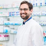 Apothecary in pharmacy standing at shelf with drugs
